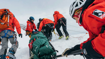 rescue team in orange jackets moving patient on litter in the snow