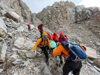 rescue team in bright jackets moving patient across rocky slope in mountains