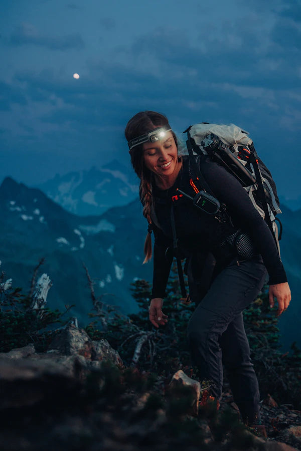 Person hiking in a mountainous area at night with a backpack and headlamp.