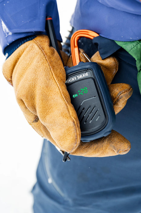Person holding a Rocky Talkie walkie-talkie in a gloved hand with a blue background