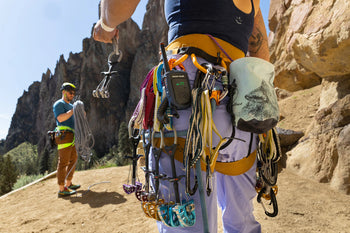 person attaching cams and trad gear to harness preparing to climb with another person coiling rope in background