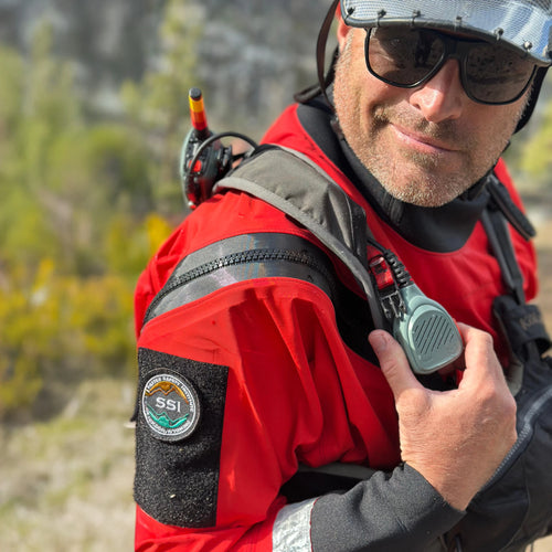 Person in a red jacket with a helmet and communication device, outdoors.