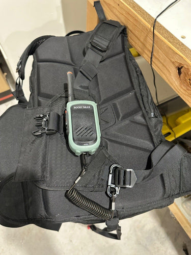 Black backpack with a walkie-talkie attached, on a light-colored floor.