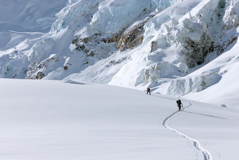 Two people hiking on a snowy mountain with a large glacier in the background