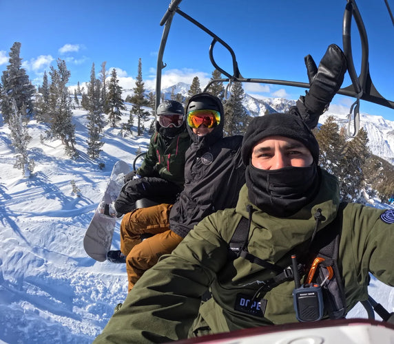 Three snowboarders on a chairlift with snowy landscape and mountains in the background