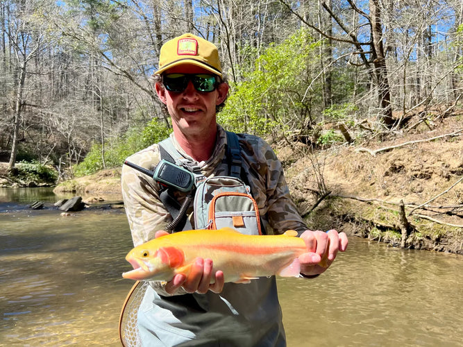 Man holding a fish by a river with trees in the background