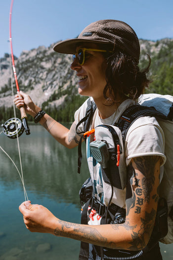 Person flyfishing in alpine lake with hat and sunglasses