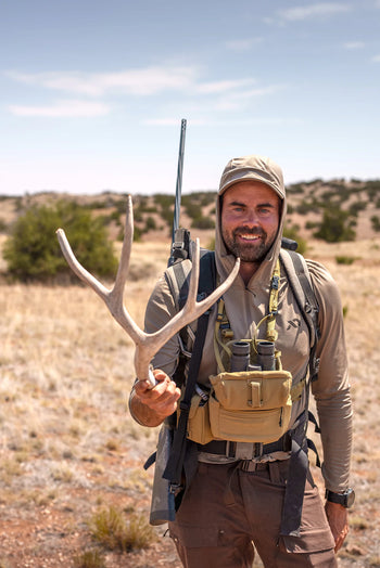 Man holding deer antlers in a desert landscape