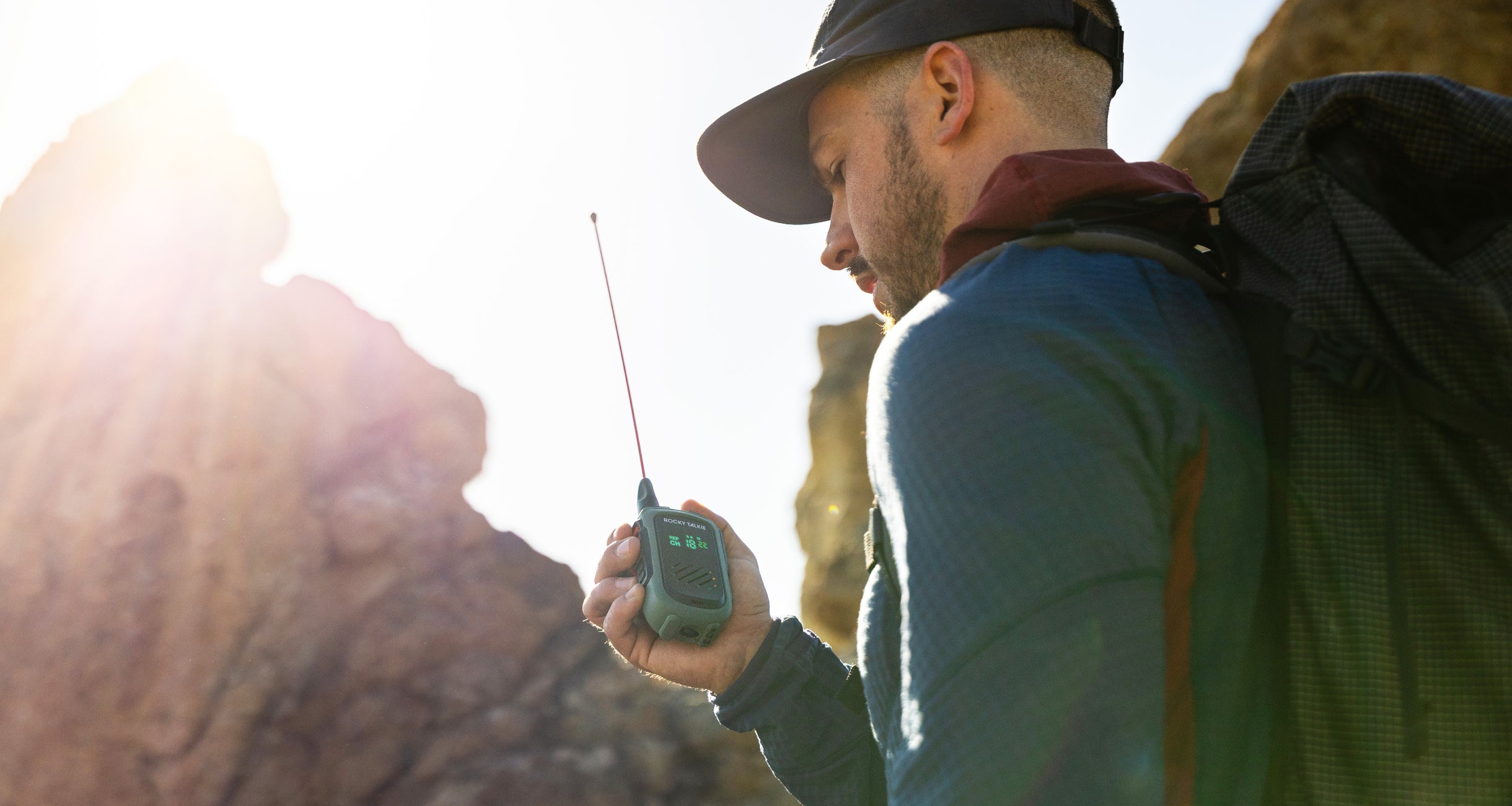 Man in outdoor setting holding a radio, surrounded by rocky landscape