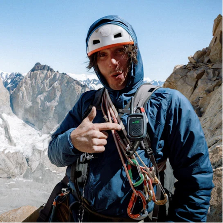 Person in climbing gear pointing at a radio with mountainous background