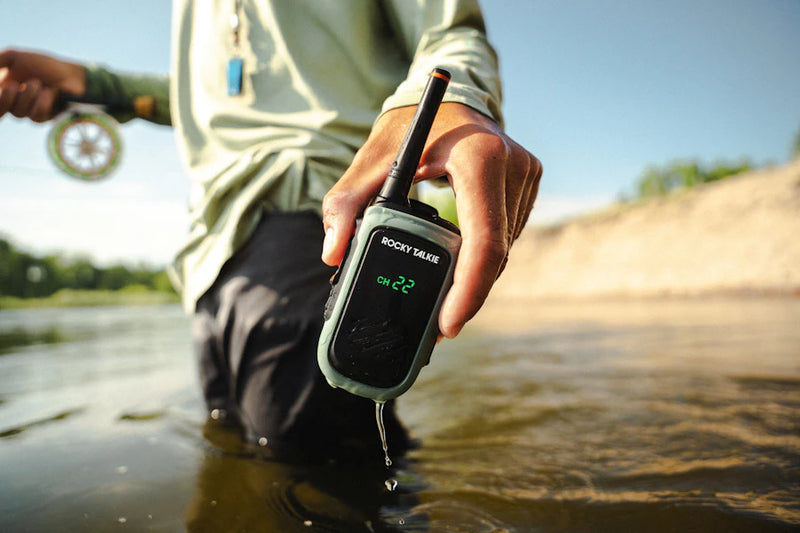 Person holding a walkie-talkie in a natural setting by a body of water