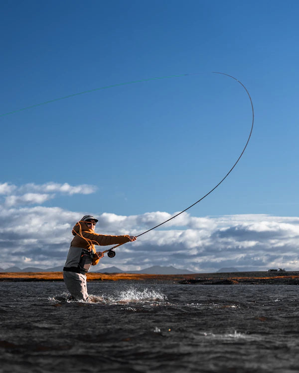 Person fly fishing in a body of water with a blue sky and clouds in the background