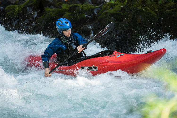 Person kayaking in white water with a red kayak and blue helmet.