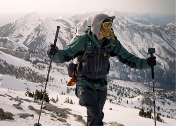 Person skiing up a snowy mountain with backpack and goggles