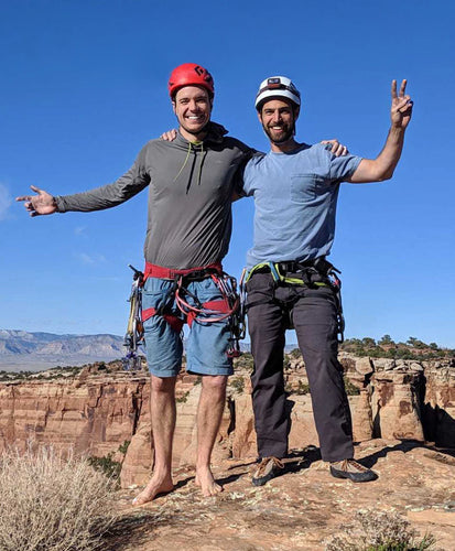 Two climbers posing on a rocky outcrop with a clear blue sky