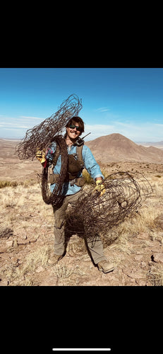 Person holding two large metal cages in a desert landscape with mountains in the background.