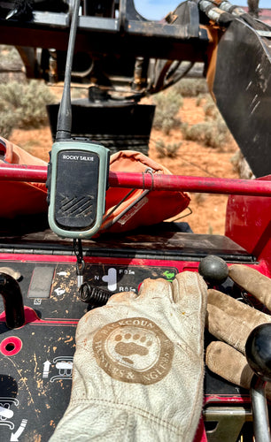 Rugged walkie-talkie on a vehicle dashboard with gloves and tools in the foreground