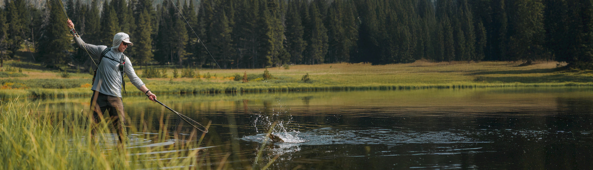 Person fly fishing in a serene lake surrounded by trees