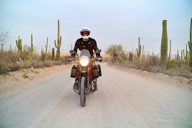 Person riding a motorcycle on a desert road with cacti in the background