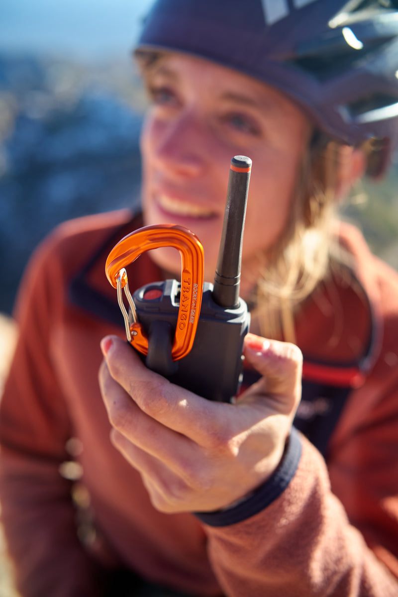 Person holding a walkie-talkie with an orange carabiner attachment outdoors
