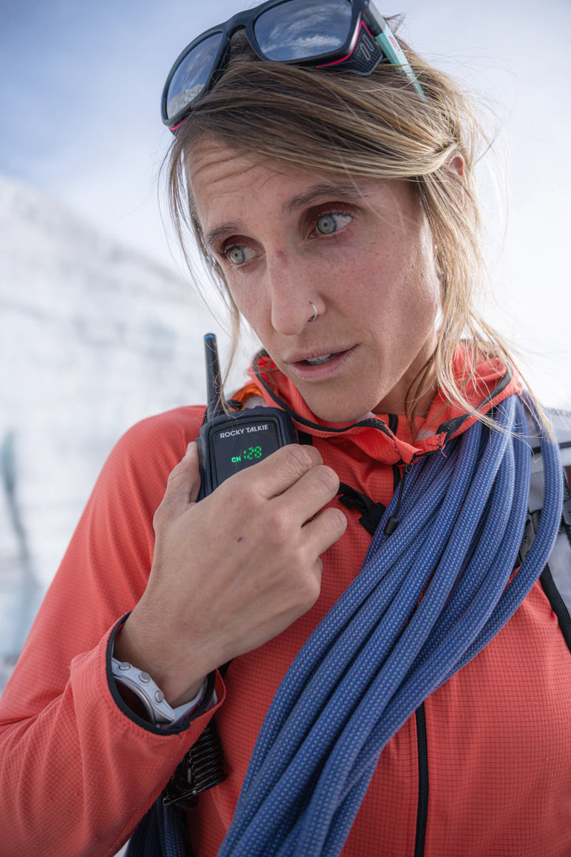 Person in red jacket with blue climbing rope, wearing sunglasses on head, in snowy landscape