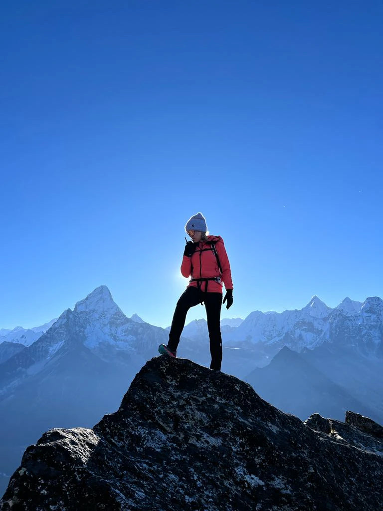 Person in a red jacket standing on a mountain peak with a clear blue sky