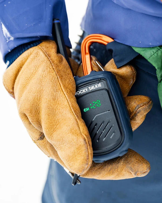 Person wearing brown gloves holding a walkie-talkie with a blue jacket in the background