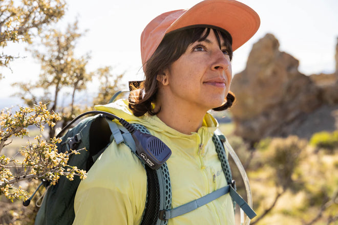 Woman hiking in a natural landscape wearing a yellow jacket and orange cap.