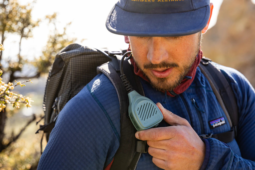Person in blue hat and sweater using hand mic on backpack shoulder strap