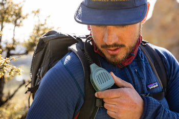 Person in blue hat and sweater using hand mic on backpack shoulder strap