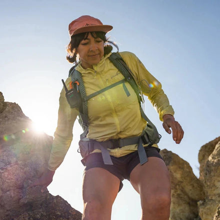 Person hiking on rocky terrain wearing a yellow jacket and red hat.