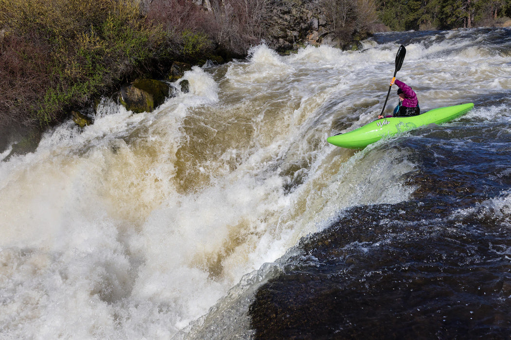 Person kayaking through a rapid on a river with rapids and trees in the background
