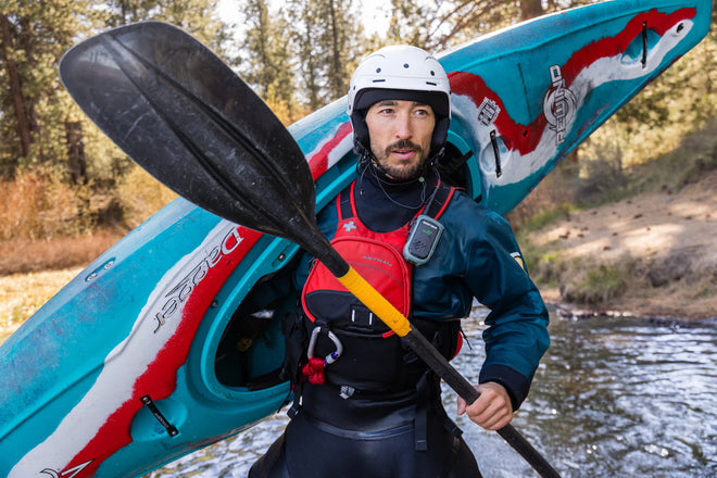Person holding a kayak and paddle with a scenic background