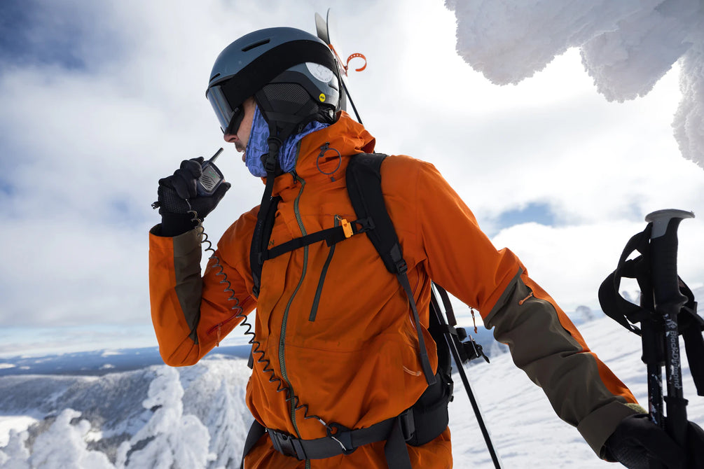 Person in orange jacket and helmet with ski equipment on a snowy mountain