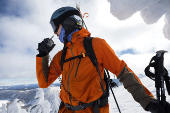 Person in orange jacket and helmet with ski equipment on a snowy mountain