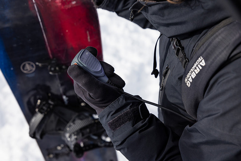 Person adjusting a snowboard with a close-up of hands wearing gloves, set against a snowy background.
