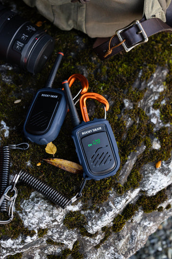 two mountain radios on mossy rock with camera and bag