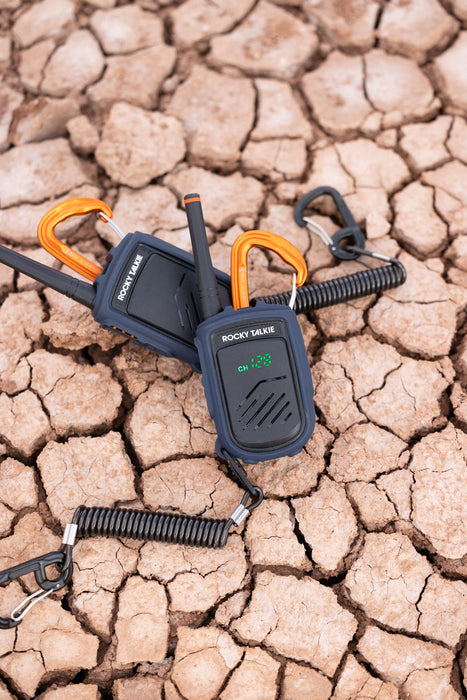 Two Rocky Talkie radios with leashes on a cracked, dry ground