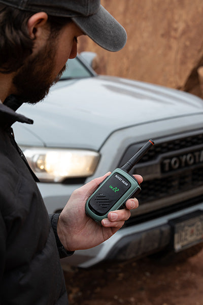 Person holding a walkie-talkie in front of a Toyota vehicle
