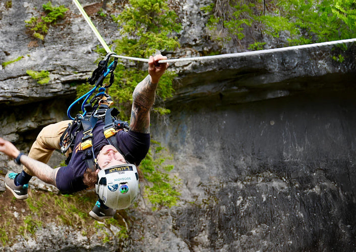 Person zip lining through a forest with rocky cliffs.