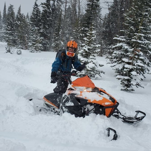 Person on an orange snowmobile in a snowy forest