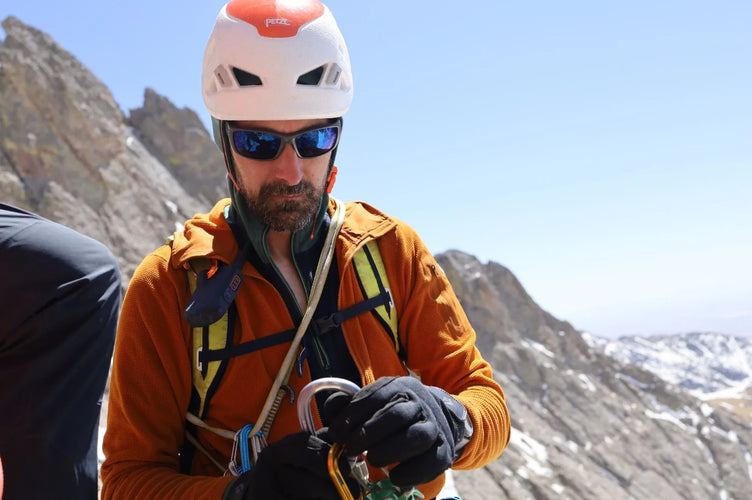 Person in orange jacket and helmet on a mountain with climbing equipment